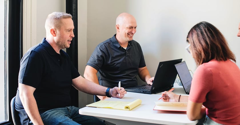 Three Vye employees sit at table with notepads and laptops