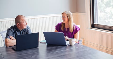 Two Vye team members talk while sitting at their computers