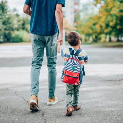 Dad and son with backpack walk hand in hand down street