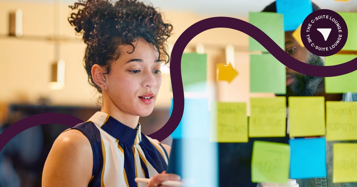 Female c-suite leader looks at wall with green post-it notes