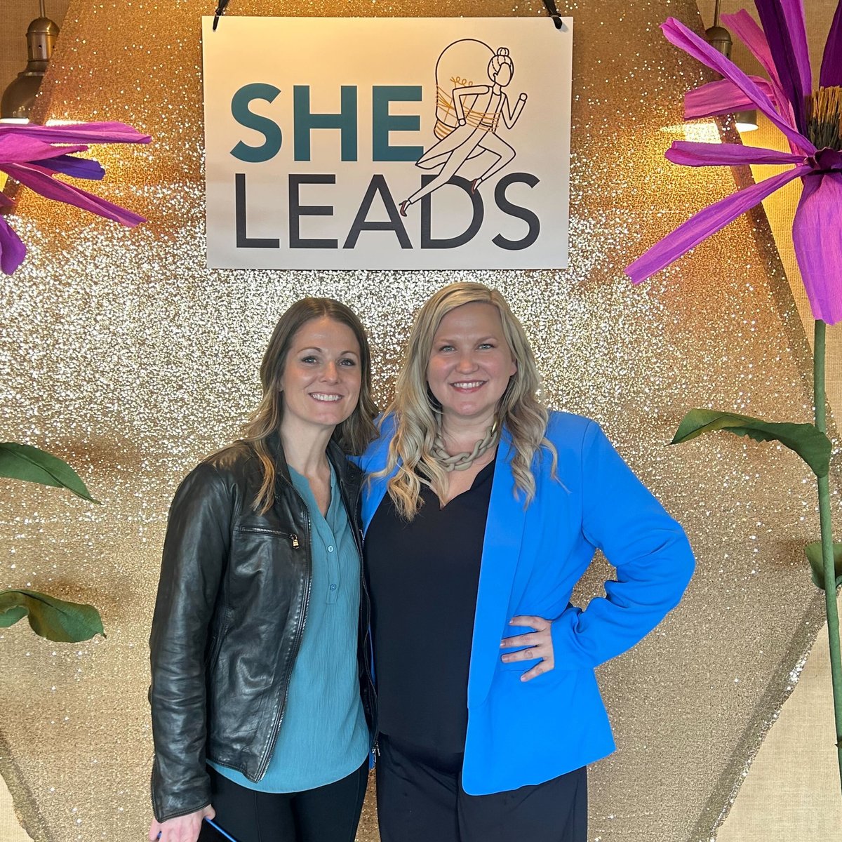 Sarah Cords and Jen Lawrence stand in front of She Leads sign in Brainerd. 