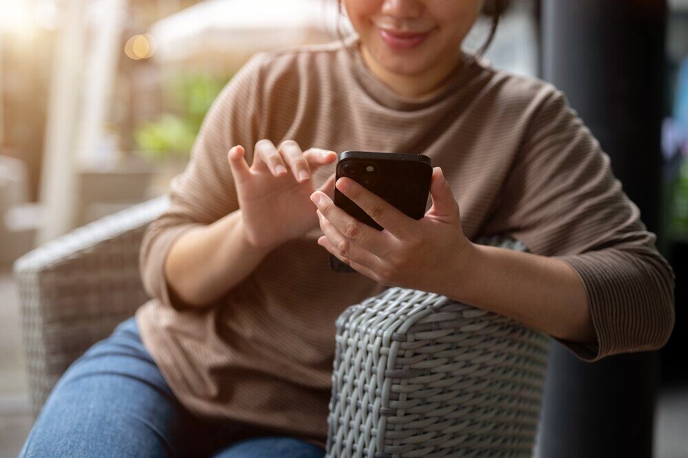 Woman sitting on chair smiles at phone while checking her emails.
