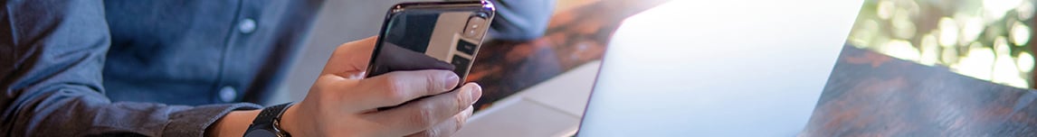 person holding a smart phone next to a laptop computer