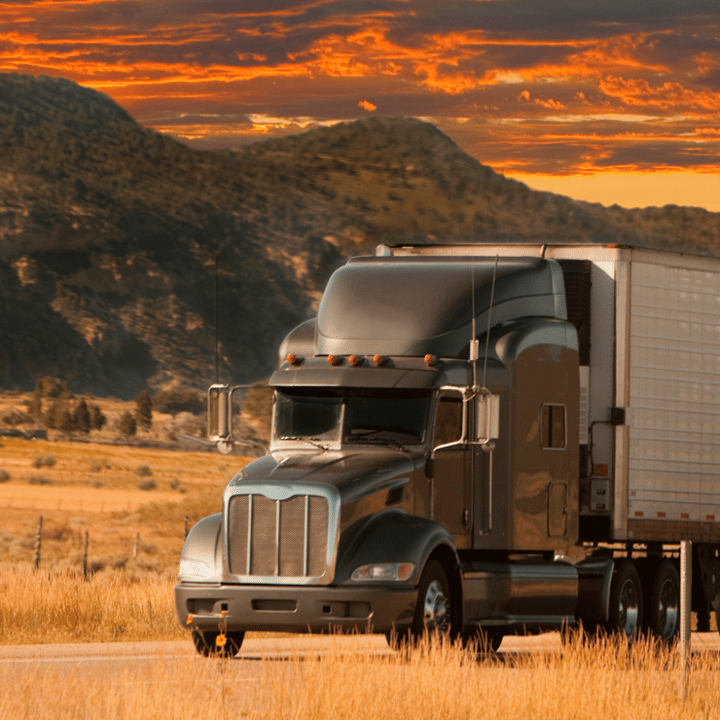 Large semi truck drives through mountains during sunset.