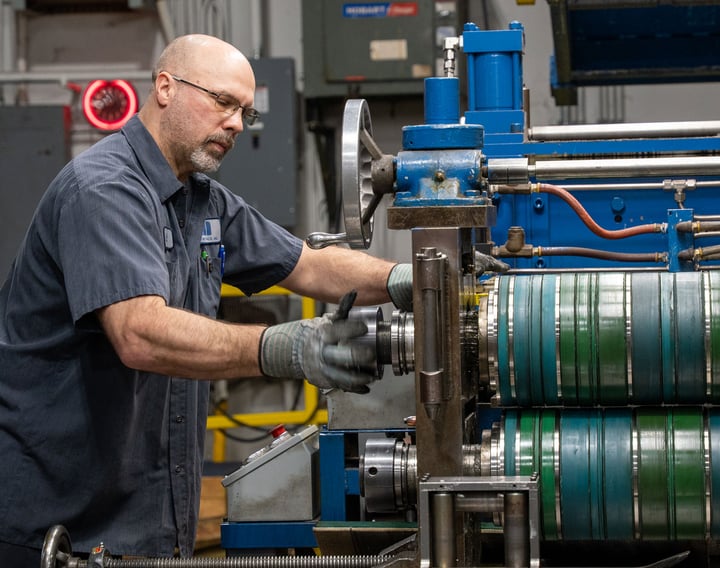 Mead Metal worker wears gloves while working with large cylinder in factory.
