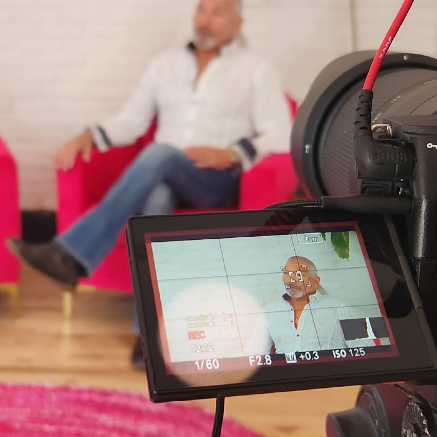 A camera screen shows the background, where a man sits in a hot pink chair